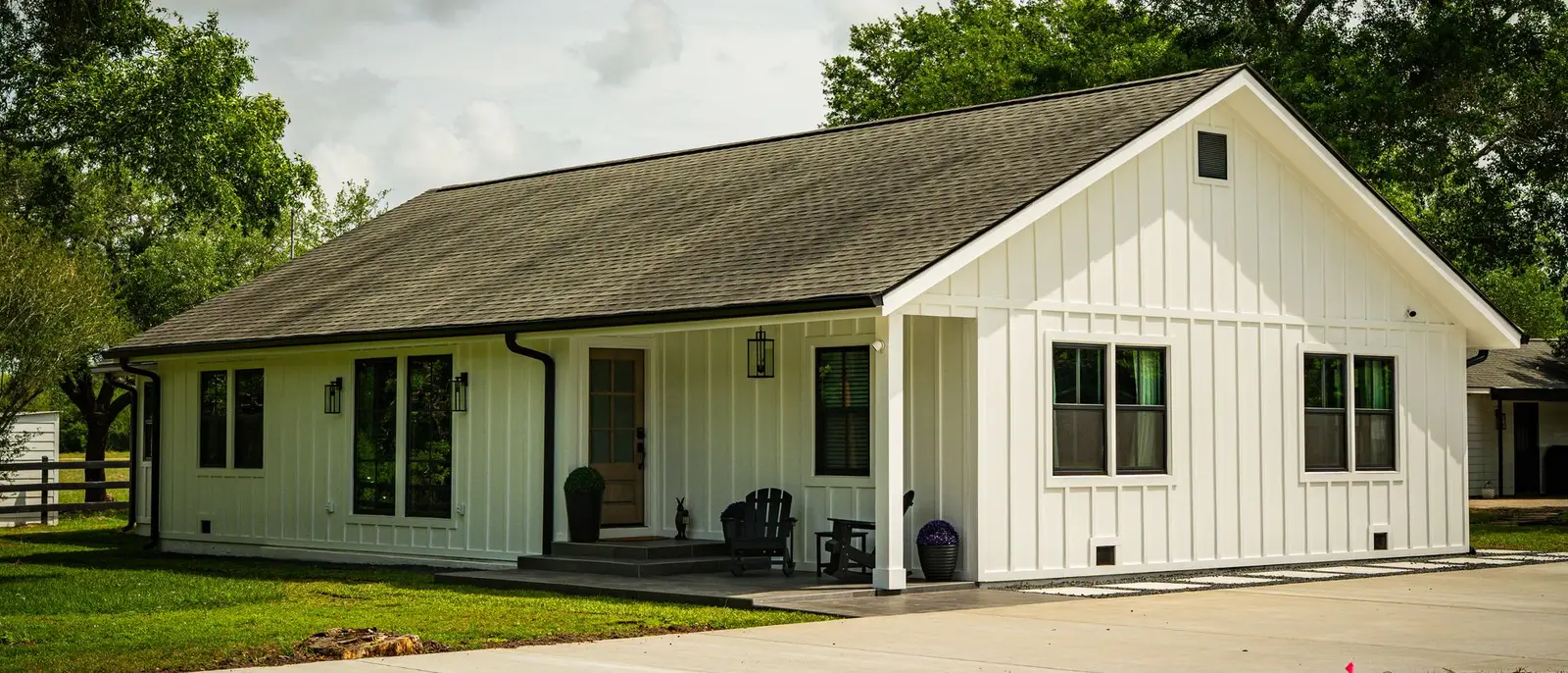 Single-story farmhouse with white board-and-batten siding, a dark shingle roof, and black-framed windows