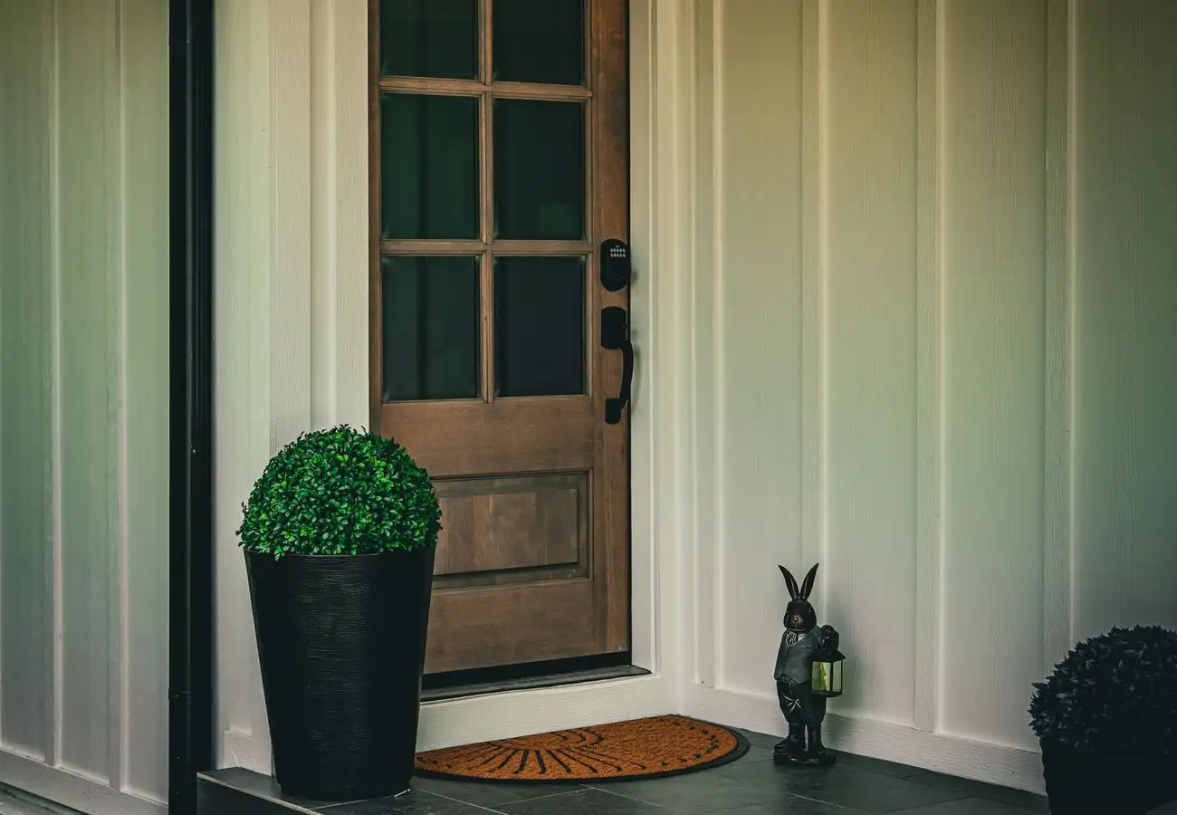 Wood front door with glass panes and a black keypad lock, set in white board-and-batten siding